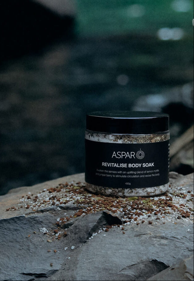 Aspar revitalise body soak jar on a rocky surface with a blurred natural background