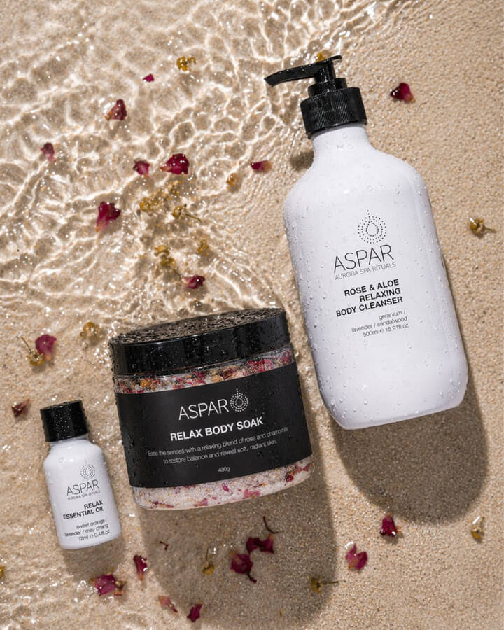 Aspar skincare products on a sandy background with flowers