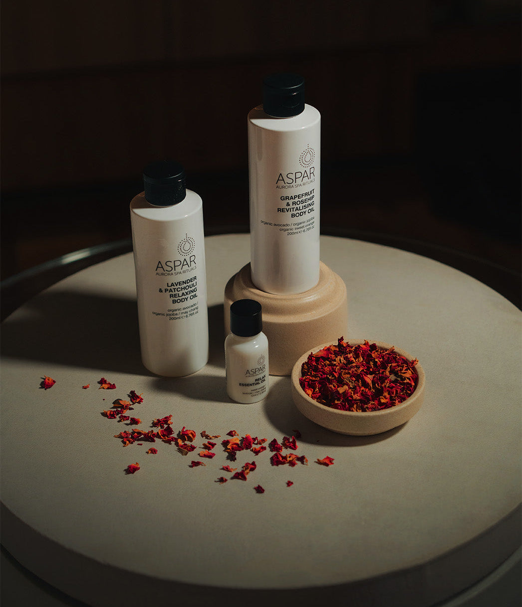 Aspar skincare products on a round surface with red dried flowers.