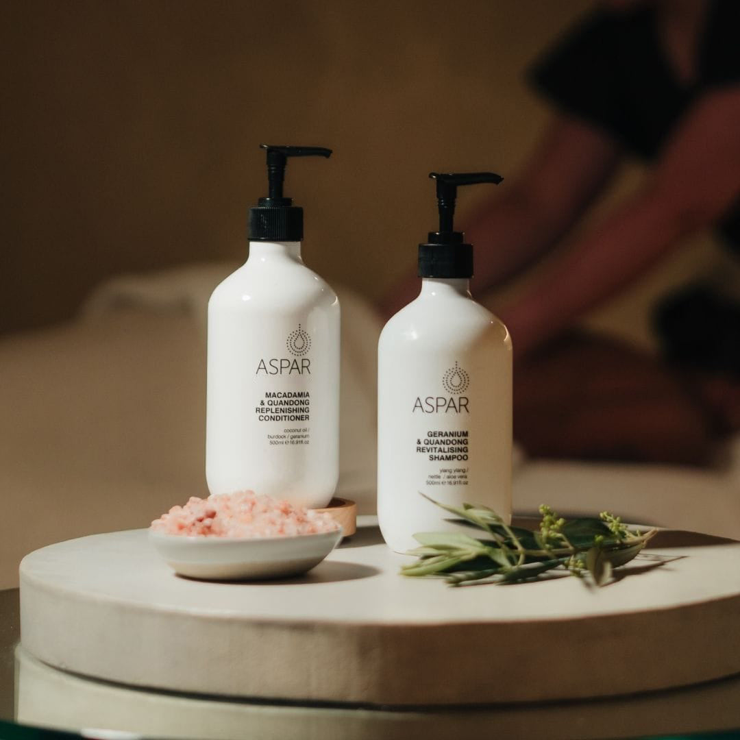 Two ASPAR hair care products on a wooden surface with a blurred background