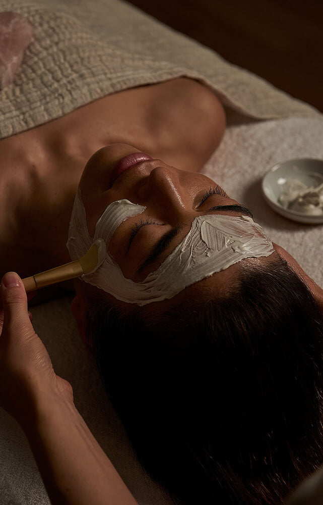 Person receiving a facial treatment with a brush applying cream to their face.