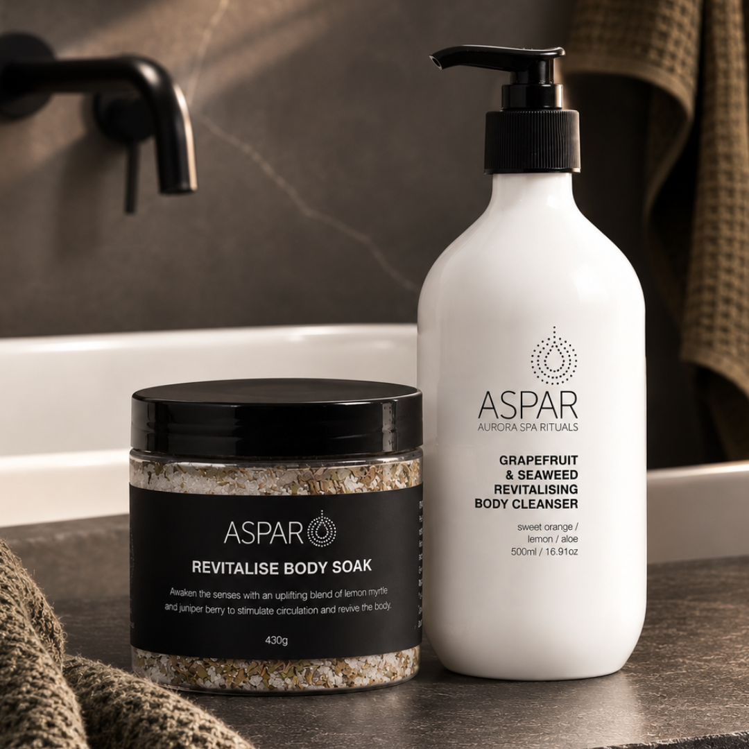ASPAR body care set featuring a jar of Revitalise Body Soak and a pump bottle of Grapefruit & Seaweed Revitalising Body Cleanser, styled on a dark stone countertop with a towel in the background.