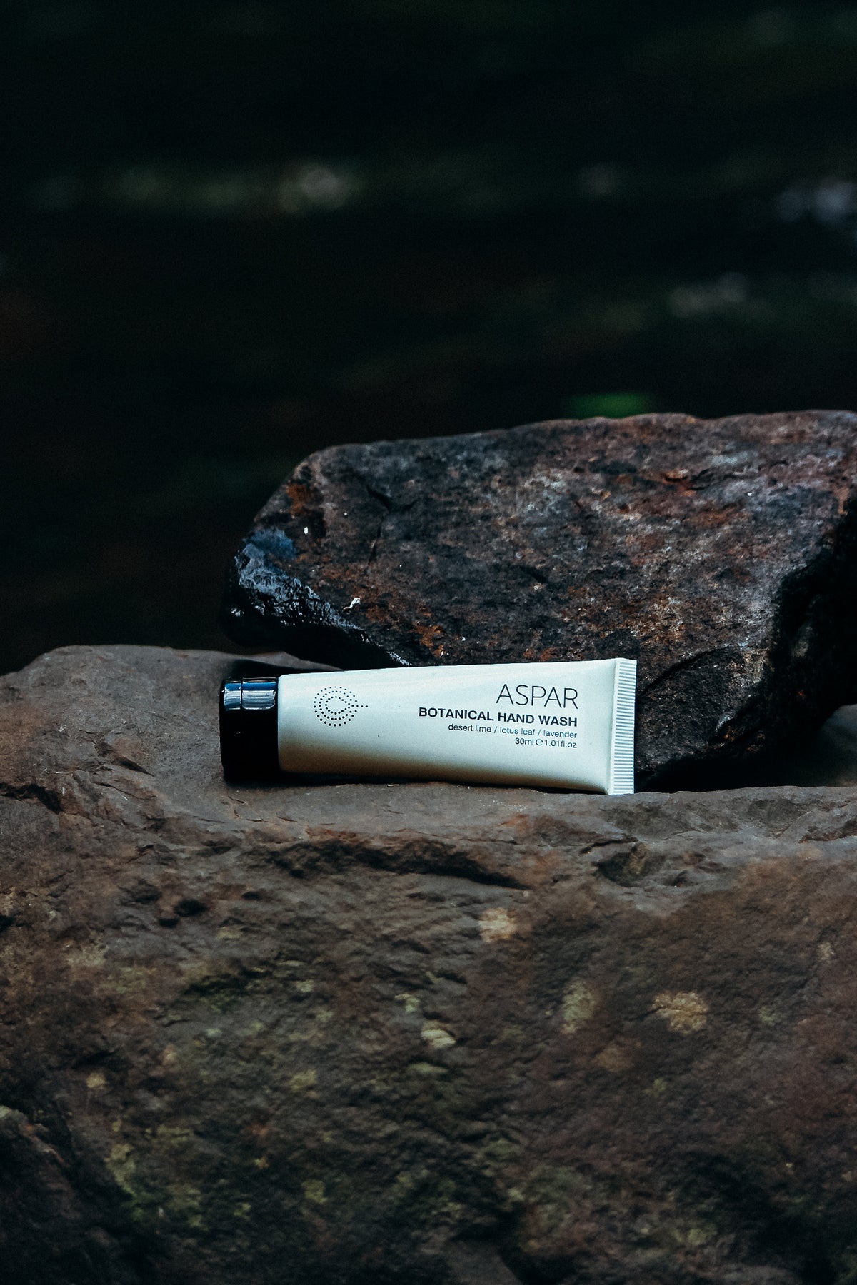 Tube of ASPAR botanical hand wash on a rock with a dark background
