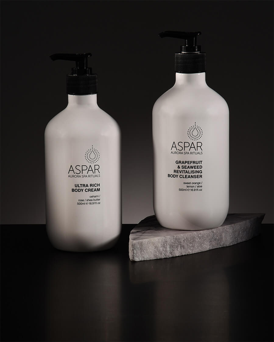 Two bottles of Aspar body care products on a dark background