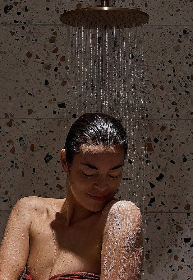 Person showering with a rain shower head in a tiled bathroom.