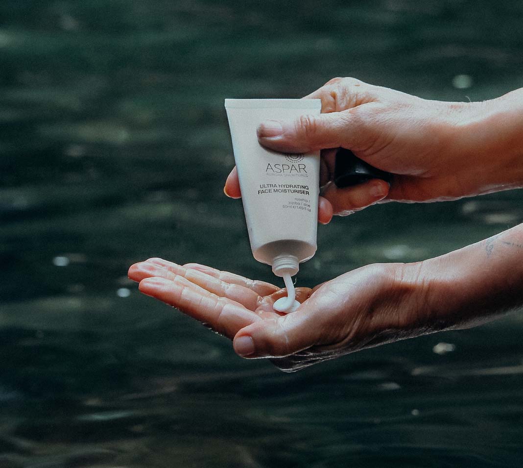 Person applying Aspar facial product to their hand with a blurred natural background
