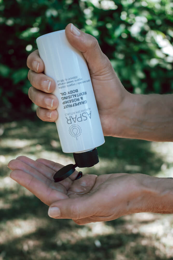 Person holding a white bottle labeled 'ASPAR' with a green outdoor background