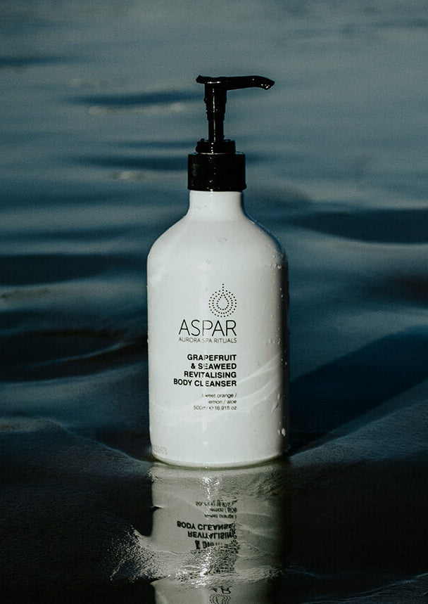 White bottle of Aspar body cleanser with pump on a reflective water surface
