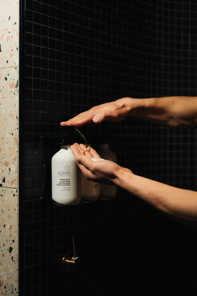 Person applying soap from a dispenser in a bathroom.