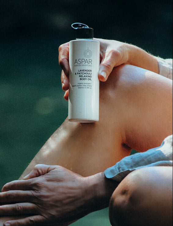 Person holding a bottle of Aspar lavender and peppermint relaxing body oil by a body of water.