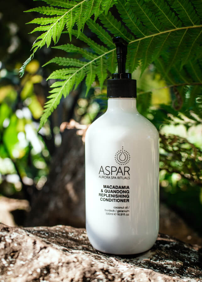 White bottle of Aspar conditioner on a tree branch with green leaves in the background