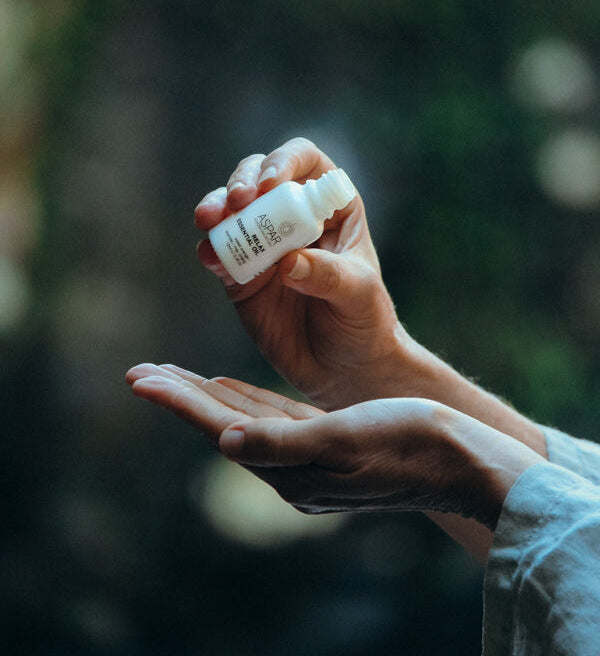 Hand holding a small bottle over another hand with a blurred natural background