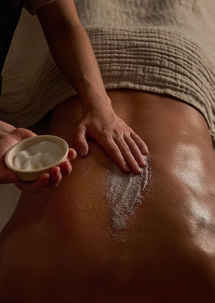 Person applying a white cream or lotion to another person's back with a bowl.