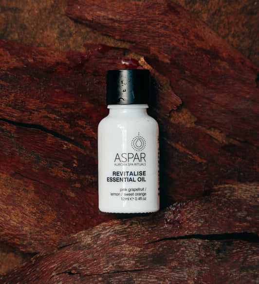 White bottle of Aspar Revitalise Essential Oil on a wooden surface