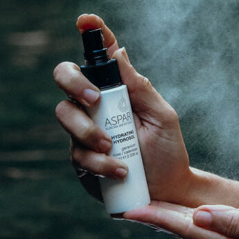 Person holding a spray bottle with mist against a blurred natural background