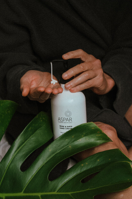 Person holding a white bottle labeled 'ASPAR' with green leaves in the foreground