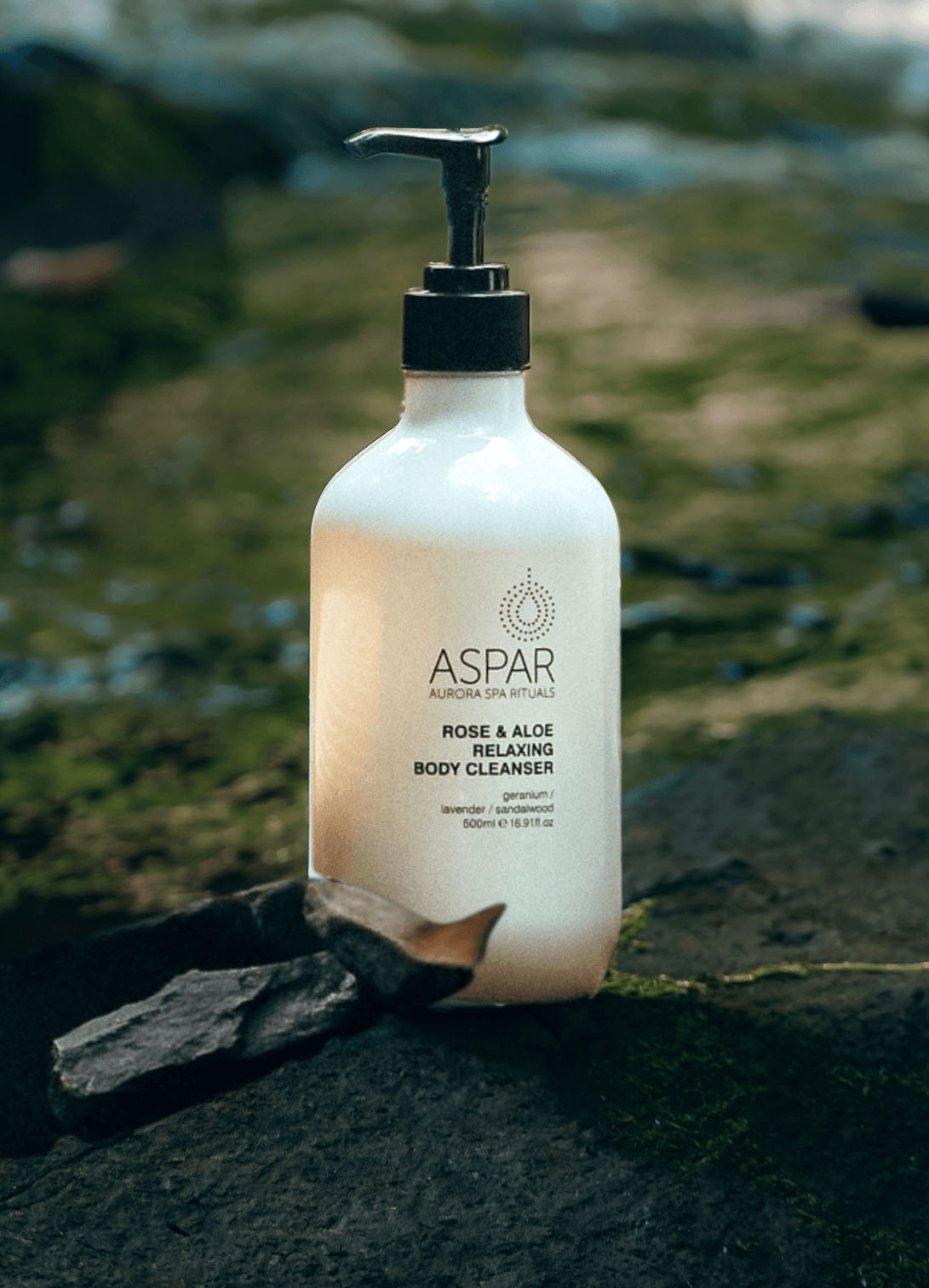 White bottle of Aspar body cleanser with pump on a natural stone surface