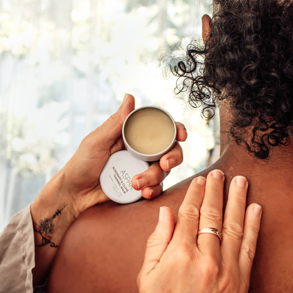 Person applying a skincare product to another person's shoulder outdoors.