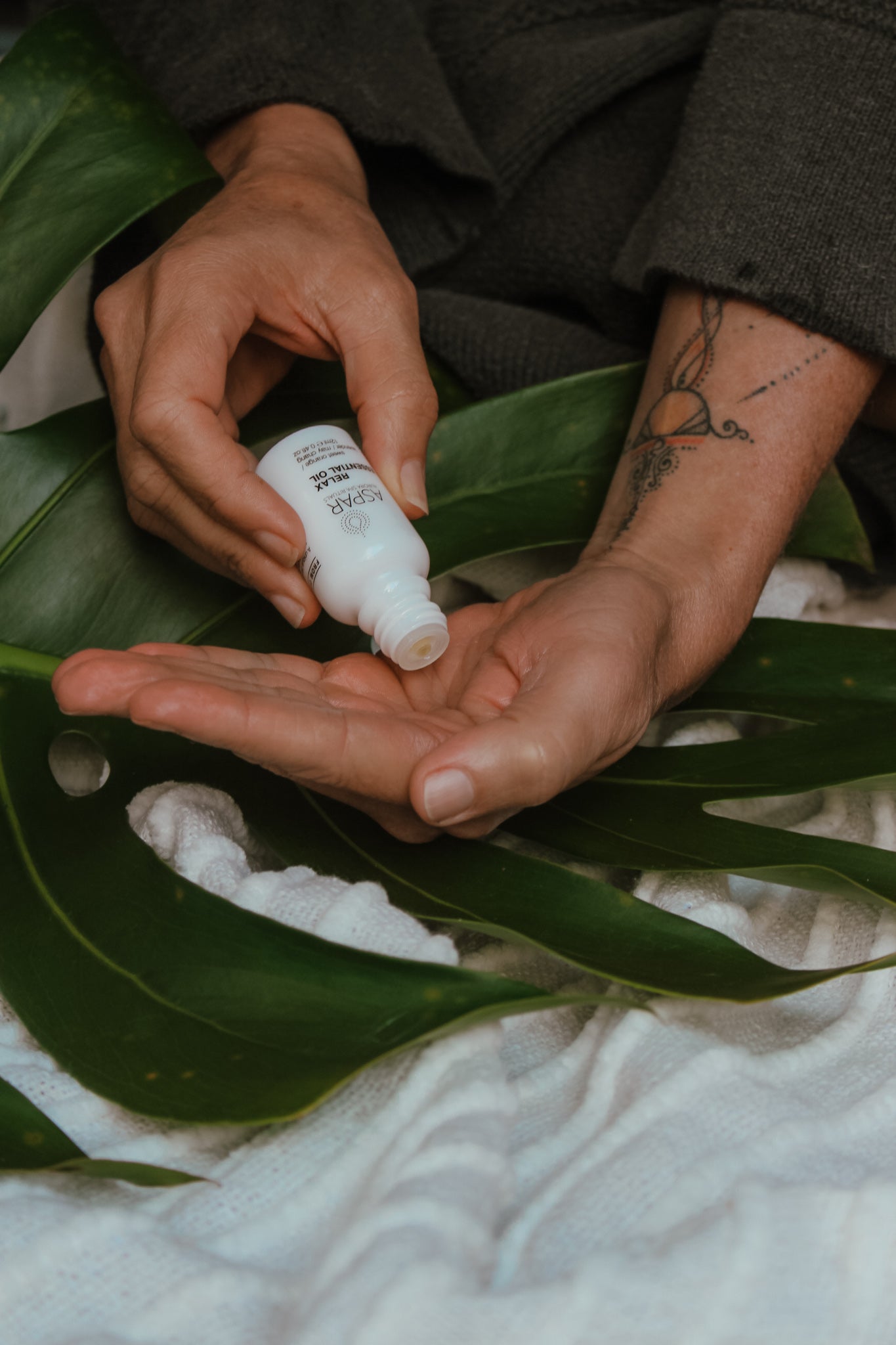 Person holding a white bottle with green leaves and fabric in the background