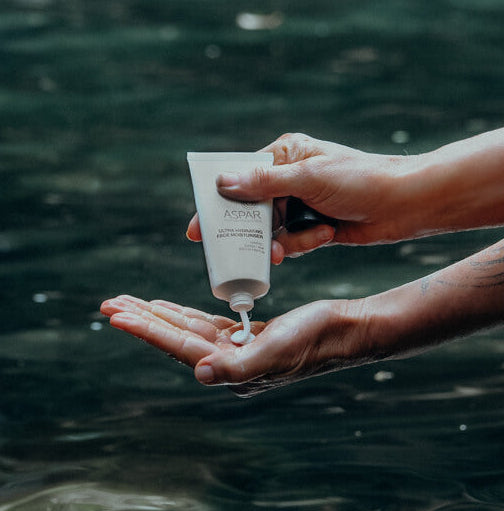 Person applying cream from a tube to their hand with water in the background