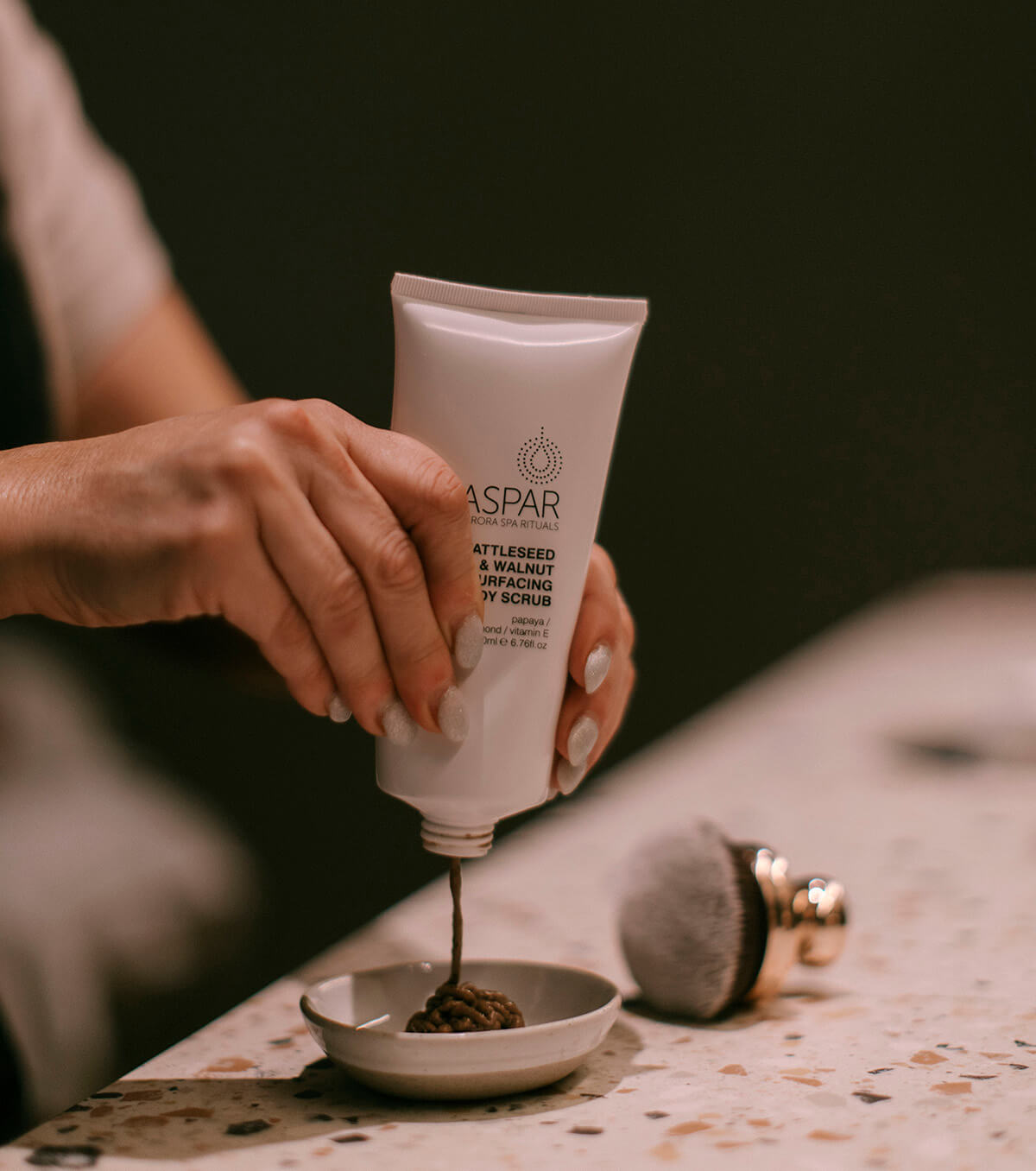Person holding a tube of Aspar scrub and applying it to a bowl.