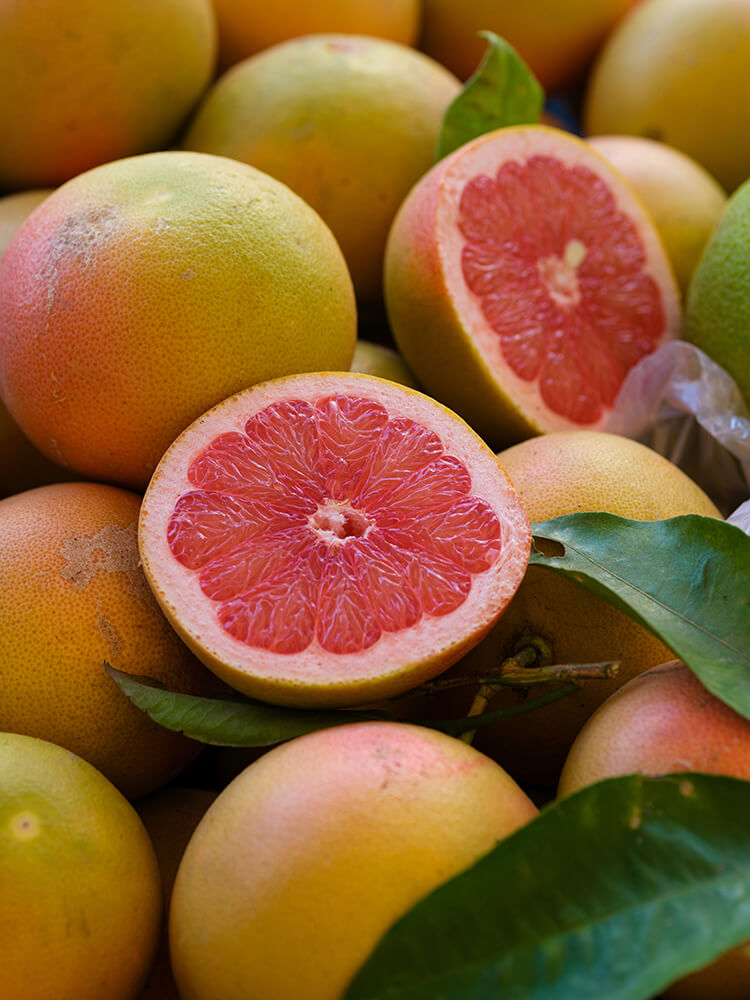 Close-up of pink grapefruits with one cut open, surrounded by green leaves.